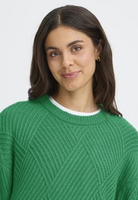 Pulover tricotat verde, cu un model texturat ce prezintă linii diagonale. Designul cu gât rotund are manșete și tiv din material cu un model ribatat.