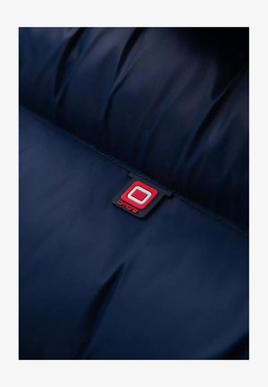 Tmavě modrá látka s jemnou texturou; obsahuje čtvercovou značkovou etiketu v červené a černé barvě, označenou "ombre", umístěnou na význačném místě.