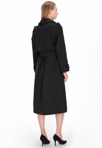 Zwarte trenchcoat met een tailleriem, een dubbele sluiting aan de voorkant en een lengte tot halverwege de kuit, met een gladde textuur en grote knoopaccenten.