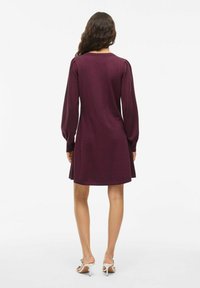 Vestido de punto burdeos con mangas largas abullonadas, escote redondeado y dobladillo acampanado. Textura suave y diseño sencillo.