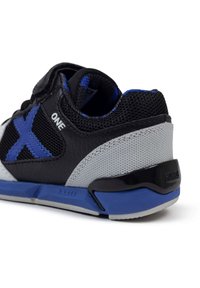 Zapatilla deportiva negra con acentos azules, paneles de malla, parte superior de cuero, talón texturizado gris y suela de goma gris con marca en la parte trasera.