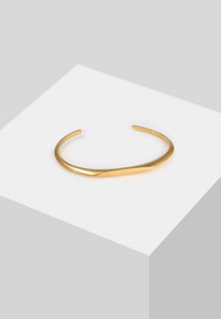 Bracciale a maniche color oro realizzato in metallo liscio con un design elegante e curvo. Le estremità aperte creano un aspetto minimalista.