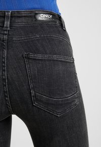 Primer plano de una persona que lleva puestos unos pantalones vaqueros negros con un bolsillo trasero y una etiqueta negra que dice ONLY sobre la cinturilla.