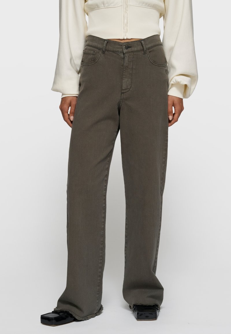 Person trägt locker sitzende, hoch taillierte graue Jeans mit ausgefransten Säumen, kombiniert mit schwarzen Schuhen mit quadratischer Spitze und einem cremefarbenen, kurz geschnittenen Hoodie.