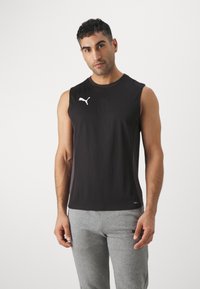 Zwarte mouwloze sporttop met een ronde hals en een wit Puma-logo op de borst, gecombineerd met lichtgrijze joggingbroek. Soepele stofstructuur.