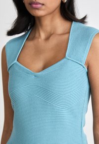 Top fitted senza maniche di colore azzurro chiaro con scollatura a V e motivi a coste testurizzati. Le caratteristiche di design notevoli includono un dettaglio sulle spalle a forma quadrata.