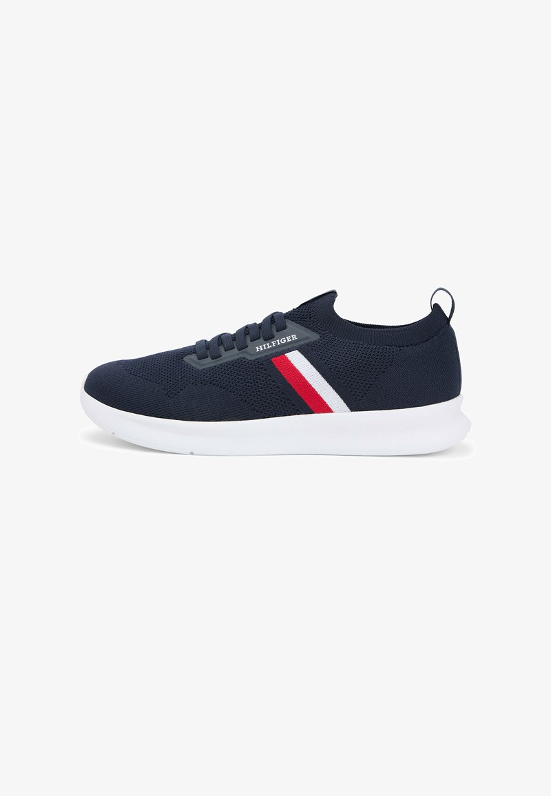 Granatowy dzianinowy sneaker z białymi i czerwonymi paskami, białą podeszwą, sznurowanym przodem oraz logo "Hilfiger" po boku.