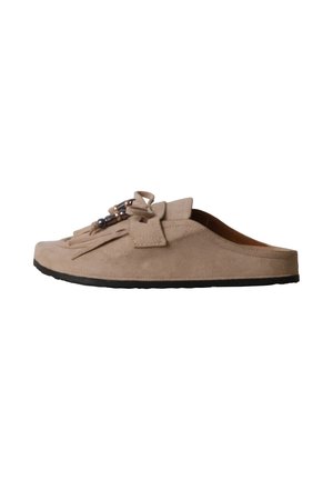 Mocassin beige en daim à enfiler avec semelle noire, pompons à l'avant, nœud et perles décoratives sur fond blanc.
