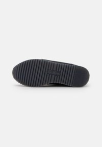 Schwarze Gummisohle eines Sneakers mit horizontalen Rillen und Logo-Prägung. Flaches Design, das die strukturierte Oberfläche für besseren Halt zeigt.