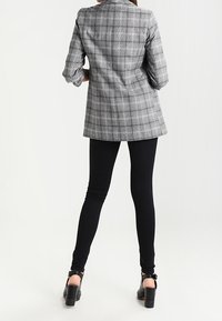 Šedý kostkovaný blazer s ohrnutými rukávy přes černé legíny a na vysokých podpatcích. Blazer má strukturovaný design a dokonale střihaný střih.