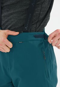 Teal utomhusbyxor med justerbara remmar, en ficka med dragkedja på sidan, slät textur och förstärkt midja med kardborreknäppning.