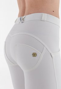 Pantalons blancs ajustés en matériau lisse et extensible, avec un design de poche arrière courbée et un petit accent logo doré.
