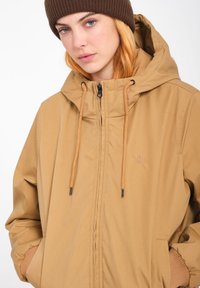 Lichtbruine hoodie met ritssluiting, verstelbare trekkoorden, elastische manchetten en zijzakken. Heeft een klein logo op de borst.