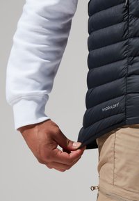 Donkerblauwe gewatteerde vest met een gequiltde textuur, voorzien van een merketiket "HYDROLOFT," gedragen over een wit langslavia-shirt, aangevuld met kaki broek.