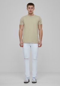Tricou bej cu mâneci scurte, asortat cu blugi skinny albi, sfâșiați, și adidași gri cu accente negre și albastre.