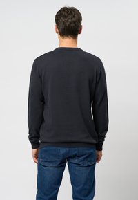 Zwarte lange mouwen trui met ronde hals en geribde manchetten, gecombineerd met blauwe denim jeans met achterzakken.