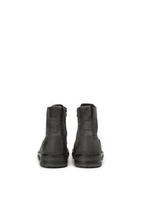 Botines de ante negro con un acabado suave, cremalleras laterales, punteras redondeadas y suelas de goma. Costuras mínimas y sin herrajes visibles.