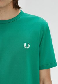 T-shirt verde in cotone con scollatura rotonda e maniche corte. Presenta un piccolo logo di alloro bianco ricamato sul petto.