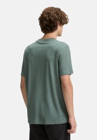 Grøn kortærmet T-shirt lavet af blødt materiale, med rund hals og afslappet pasform. Bagviewet viser minimal detaljering og glat tekstur.