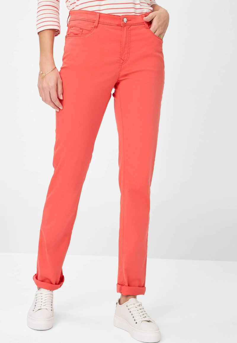 Pantalons de couleur corail avec une coupe slim, en coton, dotés de poignets retroussés, de poches avant et d'une fermeture à boutons. Associés à des baskets blanches.
