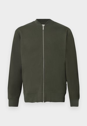 Grønn bomberjakke med full frontglidelås, ribbestrikkede mansjetter og hem. Har en jevn tekstur og minimalistisk design.