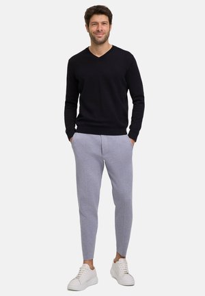 schwarzer V-Ausschnitt-Pullover kombiniert mit hellgrauen, schmal zulaufenden Jogginghosen mit vorderen Nähten und weißen Sneakers. Einfaches und modernes Design.