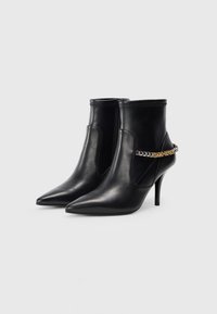 Bottines en cuir noir avec des orteils pointus, dotées d'un talon haut et d'un accent en chaîne métallique sur le côté pour un détail supplémentaire.