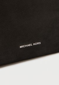 Fekete bőr kézitáska texturált felülettel, modern stílusú ezüst "MICHAEL KORS" logóval. Kompakt és elegáns kialakítás.