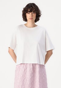 Hvit kortermet cropped t-skjorte laget av glatt bomull, kombinert med et teksturert lys rosa skjørt med bølgete mønster.