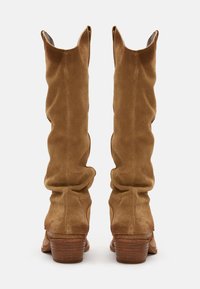 Bottes en daim marron au-dessus du genou avec un design plissé, accentuées par un talon en texture bois et un bout pointu.