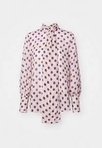 Blouse à pois en rose clair avec des pois violets foncés. Dotée d'un nœud au cou, de manches ballon longues et d'une texture côtelée tout au long.