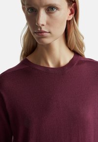 Burgundská pletená svetr s kulatým výstřihem, hladkou texturou a jemným vroubkovaným detailem na límci a ramenních švech.