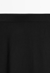 Black knitted fabric with a ribbed waistband, showing fine texture and slight folds near the seam.