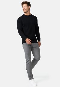 Svart strikkegenser med ribbede mansjetter og krage, kombinert med lysegrå slim-fit bukser og hvite joggesko. Viser en uformell stil.