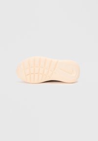 Lys beige sneakersål med et struktureret grebmønster. Har en afrundet tå og diskret branddetalje nær hælen.