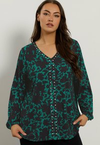 Zwarte V-halsblouse met een teal abstract patroon; heeft knoopaccenten aan de voorkant en elastische manchetten voor een ontspannen pasvorm.
