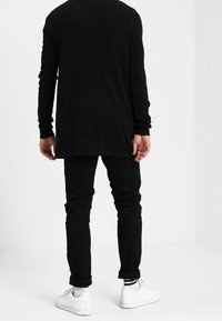 Svart långärmad tröja med ribbad struktur, bärs över svarta slim-fit byxor, kombineras med vita sneakers. Enkelt, minimalistiskt design.