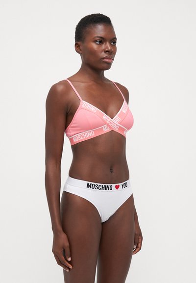 Bralet roz cu bretele groase de marcă, asociat cu chiloți albi care au un elastic cu un slogan negru și roșu. Textură netedă, design minimalist.