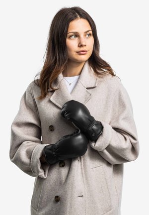 Schwarze Lederhandschuhe mit gepolstertem Design, mit gerafftem Handgelenk, getragen mit einem hellgrauen Wollmantel, der große Knöpfe und eine weiche Textur aufweist.