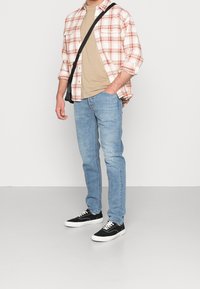 Jasnoniebieskie dżinsy, beżowy t-shirt i koszula w czerwoną i białą kratkę na guziki. Czarna torba na ramię i czarne sneakersy z białą podeszwą.