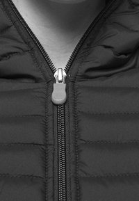 Lähikuva mustasta puhalletusta takista, jossa on näkyvä vetskari ja tikattu ompelu kaulan ja rinnan ympärillä.