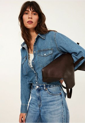 Jasnoniebieska koszula jeansowa z długimi rękawami, zapięcie na guziki z przodu, podwójne kieszenie na piersi. W połączeniu z wysokim stanem, zwietrzałymi niebieskimi dżinsami. Ciemnobrązowa skórzana torba.