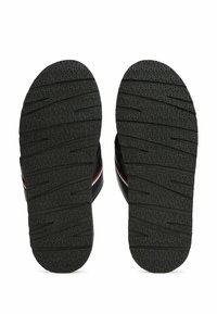 Infradito in gomma nera con una suola texture. Presentano una larga fascia con un accento rosso e bianco. Design piatto adatto per un uso casual.