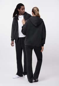 Σετ μαύρου βελουτέ φούτερ με κουκούλα και παντελόνι, με άνετη εφαρμογή, ελαστική μέση με κορδόνι και μεγάλες τσέπες. Ομαλή υφή με casual εμφάνιση.