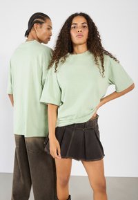 Světle zelené oversized tričko vyrobené z měkké tkaniny, s krátkými rukávy. Tmavé džínové sukně s záhyby a roztrhaným lemem. Jednoduchá obuv.