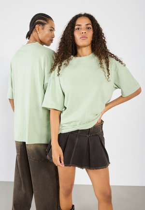 Light green oversized T-shirt made of soft fabric, with short sleeves. Dark denim skirt featuring pleats and frayed hem. Simple footwear.