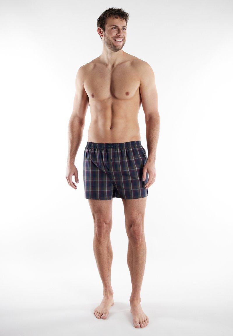 Boxer in tartan blu navy con elastico in vita, caratterizzati da strisce rosse e verdi. Realizzati in tessuto morbido, lunghi fino al ginocchio, design minimalista.