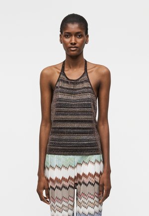 Γυναίκα που φοράει τοπ χωρίς μανίκια, με halter neck και οριζόντιες ρίγες, καθώς και παντελόνι με ψηλόμεση μέση και πολύχρωμα ζιγκ-ζαγκ μοτίβα.