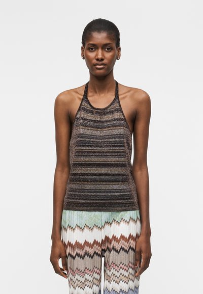 Γυναίκα που φοράει τοπ χωρίς μανίκια, με halter neck και οριζόντιες ρίγες, καθώς και παντελόνι με ψηλόμεση μέση και πολύχρωμα ζιγκ-ζαγκ μοτίβα.
