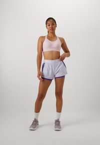 Sostén deportivo de color rosa claro, pantalones cortos blancos con acentos morados, paneles laterales de malla y cinta elástica en la cintura. Zapatillas claras y calcetines blancos de caña corta.